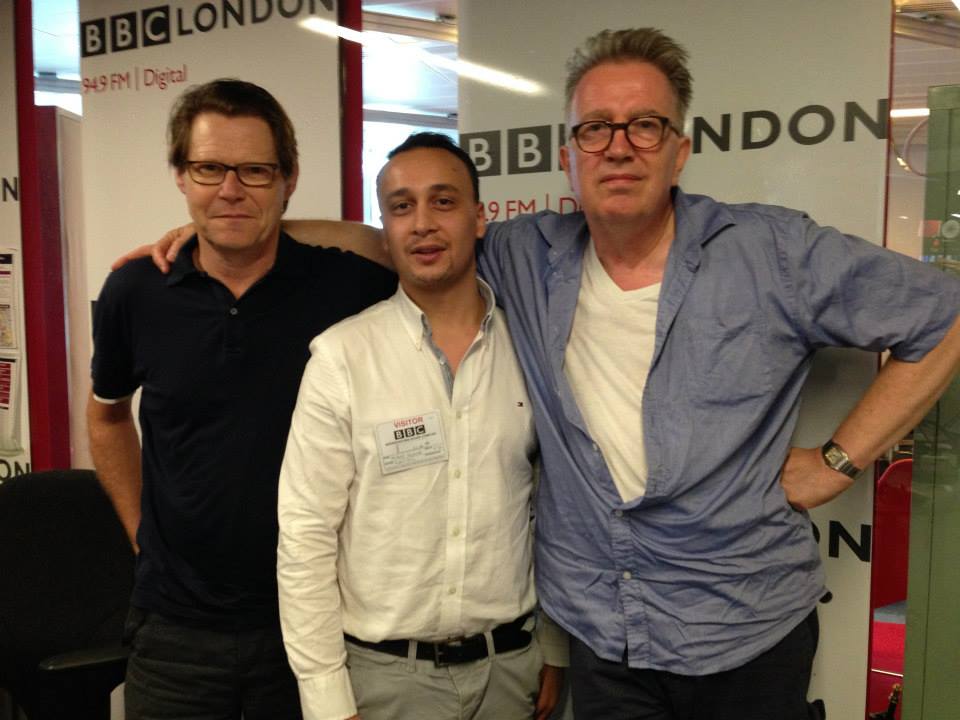 Michael Darius Eastwood wearing a BBC visitor badge, standing between Robert Elms of BBC London and Tom Robinson of BBC Radio 6 Music, in front of BBC London 94.9 FM studio branding