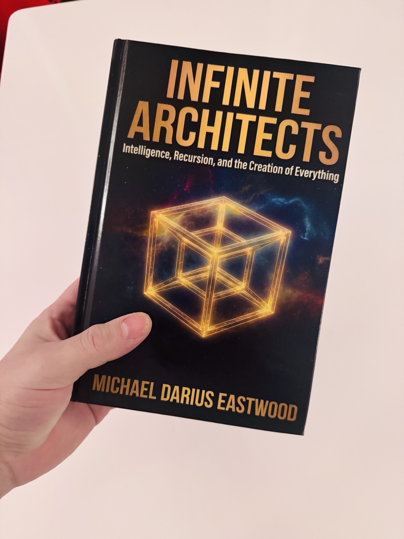 A hardback copy of Infinite Architects: Intelligence, Recursion, and the Creation of Everything by Michael Darius Eastwood, held in one hand